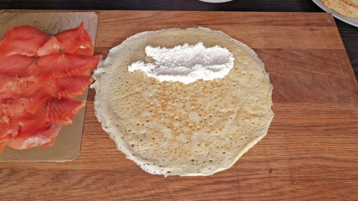 Пышный дрожжевой блин с мягким сыром, рядом ломтики красной рыбы