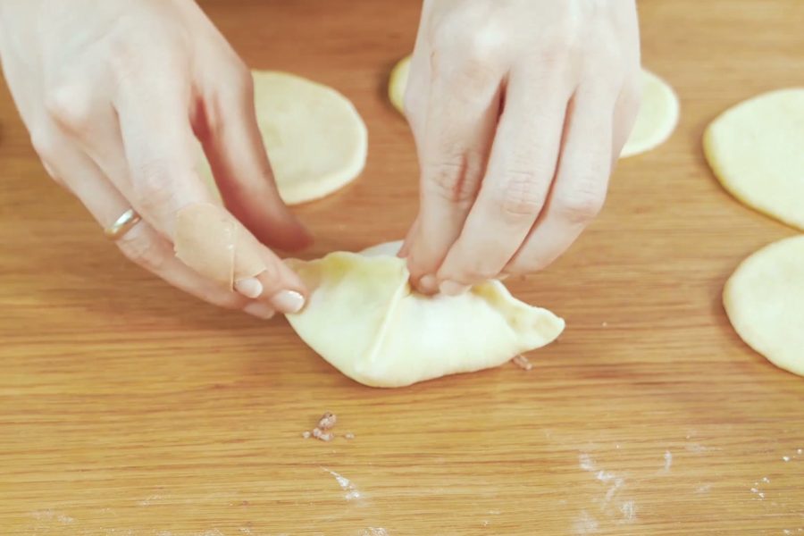 Руки защипывают квадратный пирожок с мясом