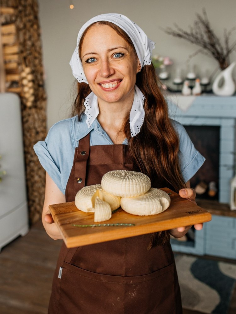 Алла Лапина в фартуке держит доску с головками домашнего сыра
