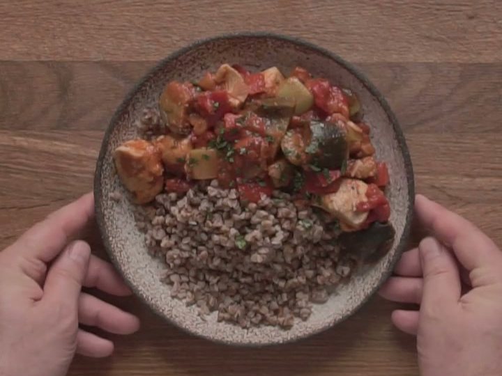 Куриный паприкаш с овощами в томатном соусе и гречка в тарелке в руках шефа