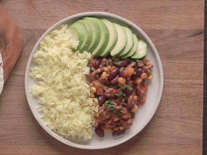 Рагу из фарша с фасолью и кукурузой, жёлтый рис и ломтики авокадо на тарелке