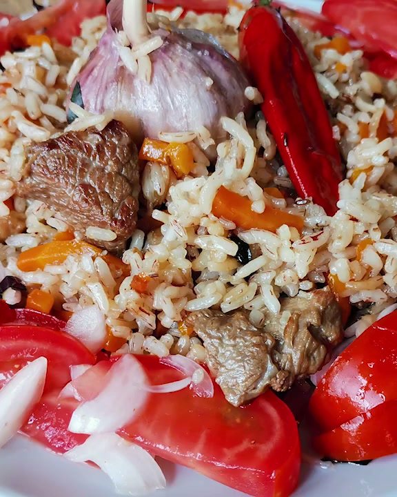 Плов с мясом, головкой чеснока и перцем, вокруг салат из помидоров с луком